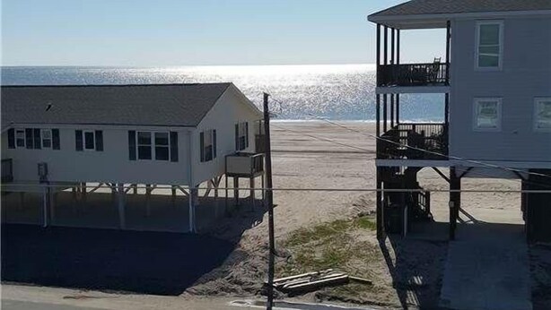 Une maison située sur la côte, dotée d’un balcon, offrant une vue sur la plage et surplombant un ciel dégagé.