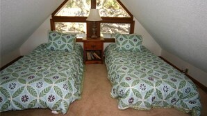 A small, triangular attic bedroom with two single beds, a nightstand, and a lamp. - Green Parrot (Edisto Island)