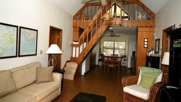 A spacious living area with a wooden staircase, a sofa, a wicker chair, and a dining table. - Green Parrot (Edisto Island)