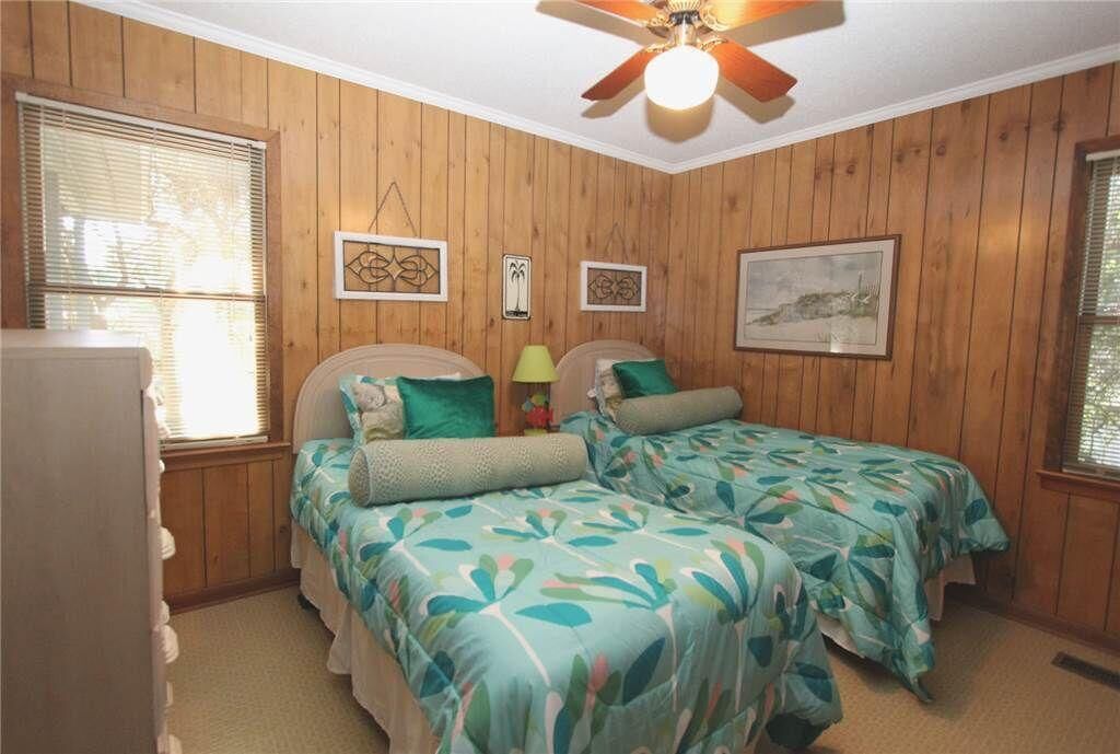 Ein Zimmer mit Holzwandverkleidung, zwei Betten mit Blumenmuster-Bettwäsche, einem Deckenventilator und Kunstwerken an den Wänden.