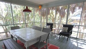 A covered outdoor dining area with a table and chairs, large windows, and hanging decorations. - Miss Irene (Edisto Island)