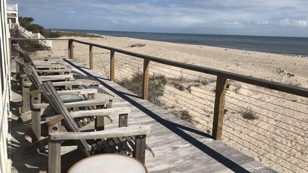 A wooden deck with beach chairs and a table overlooking a sandy beach and ocean. - Oristo (Edisto Island)
