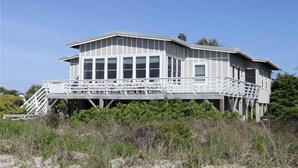 A beachfront house with a large deck, multiple windows, and a staircase leading to the entrance. - Oristo (Edisto Island)