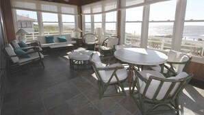 A sunlit patio with wicker furniture, large windows, and a view of the ocean. - Oristo (Edisto Island)