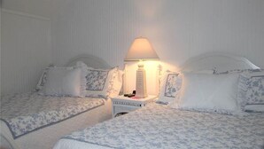 A hotel room with two beds, each with a canopy and matching headboards. There is a bedside table with a lamp between the beds.