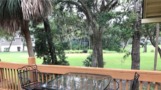 A glass-top table with metal chairs on a wooden deck, overlooking a grassy area with trees. - Palmetto Walk 333 (Edisto Island)