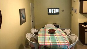 A dining area with a table covered by a plaid tablecloth, surrounded by wicker chairs. - Palmetto Walk 333 (Edisto Island)