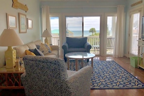 A living room with a sofa, armchair, and a round table. There is a view of the ocean through large windows. - The Retreat 5B (Edisto Island)