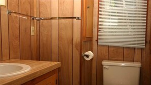 Ein Badezimmer mit Holzwänden, einer Toilette, einer Toilettenpapierrolle und einem Fenster mit Jalousien.
