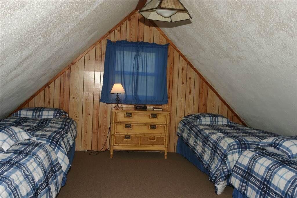 A small, cozy attic bedroom with two beds, a dresser, and a window with a blue curtain.