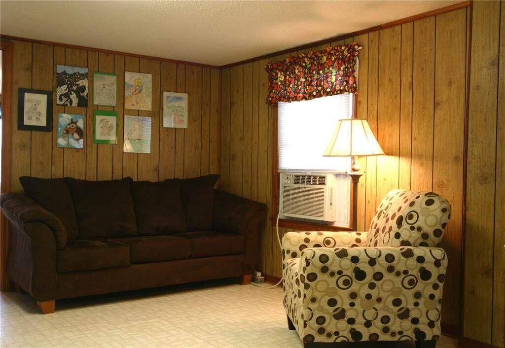 Ein Zimmer mit einem braunen Sofa, einem gemusterten Sessel und einem Fenster mit einem blumigen Vorhang.