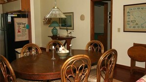 A dining room with a wooden table and chairs, a hanging lamp, and a refrigerator. - Shark's Tooth (Edisto Island)