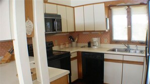 A compact kitchen with white cabinets, a microwave, a coffee maker, and a sink. - Shark's Tooth (Edisto Island)