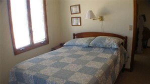 A bedroom with a wooden bed, a quilt, two wall-mounted lamps, and a window with blinds. - Shark's Tooth (Edisto Island)