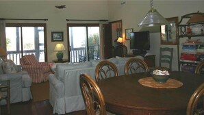 A living room with a dining table, chairs, sofas, a television, and a balcony with a view. - Shark's Tooth (Edisto Island)