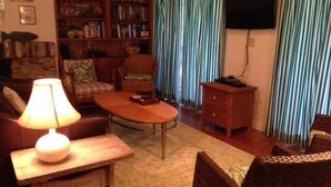 A cozy living room with a sofa, a coffee table, a bookshelf, and a television. - Shrimpers Cove (Edisto Island)