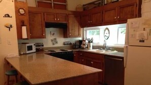 A kitchen with wooden cabinets, a central island, a microwave, a stove, and a refrigerator. - Shrimpers Cove (Edisto Island)