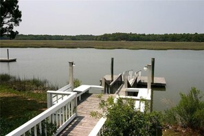 A wooden dock extending into a calm lake with a grassy shoreline and trees in the background. - Shrimpers Cove (Edisto Island)