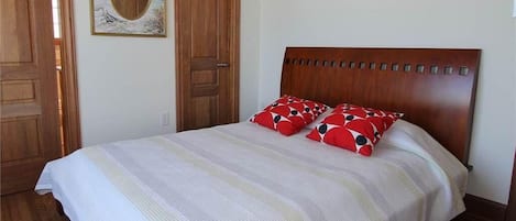 A bedroom with a wooden headboard, a bed with striped bedding, and two red pillows with black patterns.