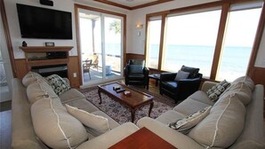 A living room with a sofa set, a coffee table, a TV mounted on the wall, and a view of the sea through large windows. - Stormy's Newhaven (Edisto Island)