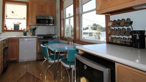 A kitchen with wooden cabinets, a microwave, a dishwasher, a small dining table with chairs, and a window with a view of the outside. - Stormy's Newhaven (Edisto Island)