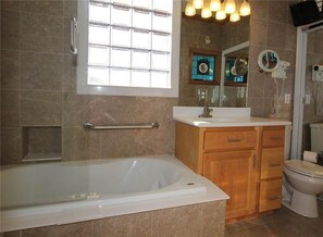 A bathroom with a bathtub, vanity, toilet, and a window with a view.