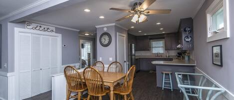 A modern kitchen with a central island, wooden dining table with chairs, and a ceiling fan.