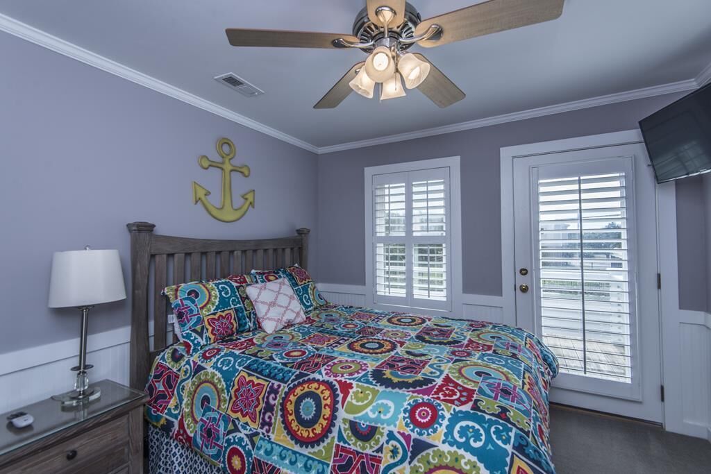 A bedroom with a bed, a ceiling fan, a nightstand, a lamp, and a TV mounted on the wall.