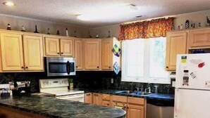 A kitchen with wooden cabinets, a stainless steel refrigerator, a microwave, and a granite countertop. - Swamp Fox (Edisto Island)