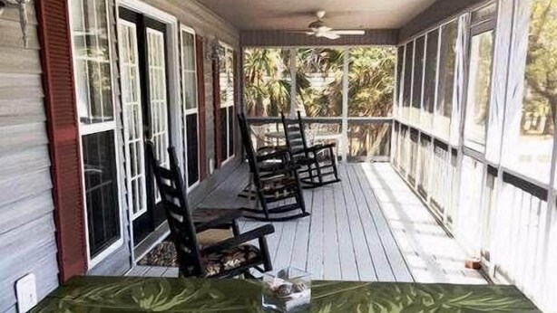 A covered porch with a wooden table and chairs, large windows, and a ceiling fan. - Swamp Fox (Edisto Island)