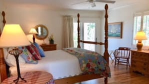 Une chambre à coucher avec un lit à baldaquin, une petite table ronde, une chaise, une commode et un ventilateur de plafond.