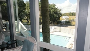 Une chambre avec vue sur une piscine, une chaise en osier blanche et une balustrade blanche.