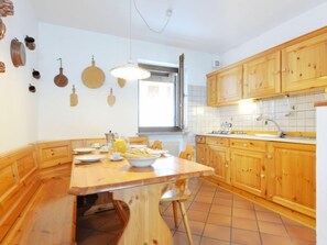 A kitchen with wooden cabinets, a tiled backsplash, and a dining table set for four. - Casa Marmolada by Interhome (Canazei)