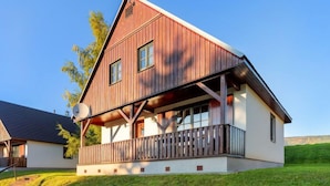 Una casa moderna de dos pisos con fachada de madera, un balcón y una antena parabólica.