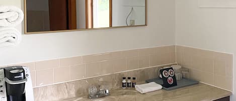 A bathroom with a sink, mirror, and towel rack. There is a coffee maker on the counter.