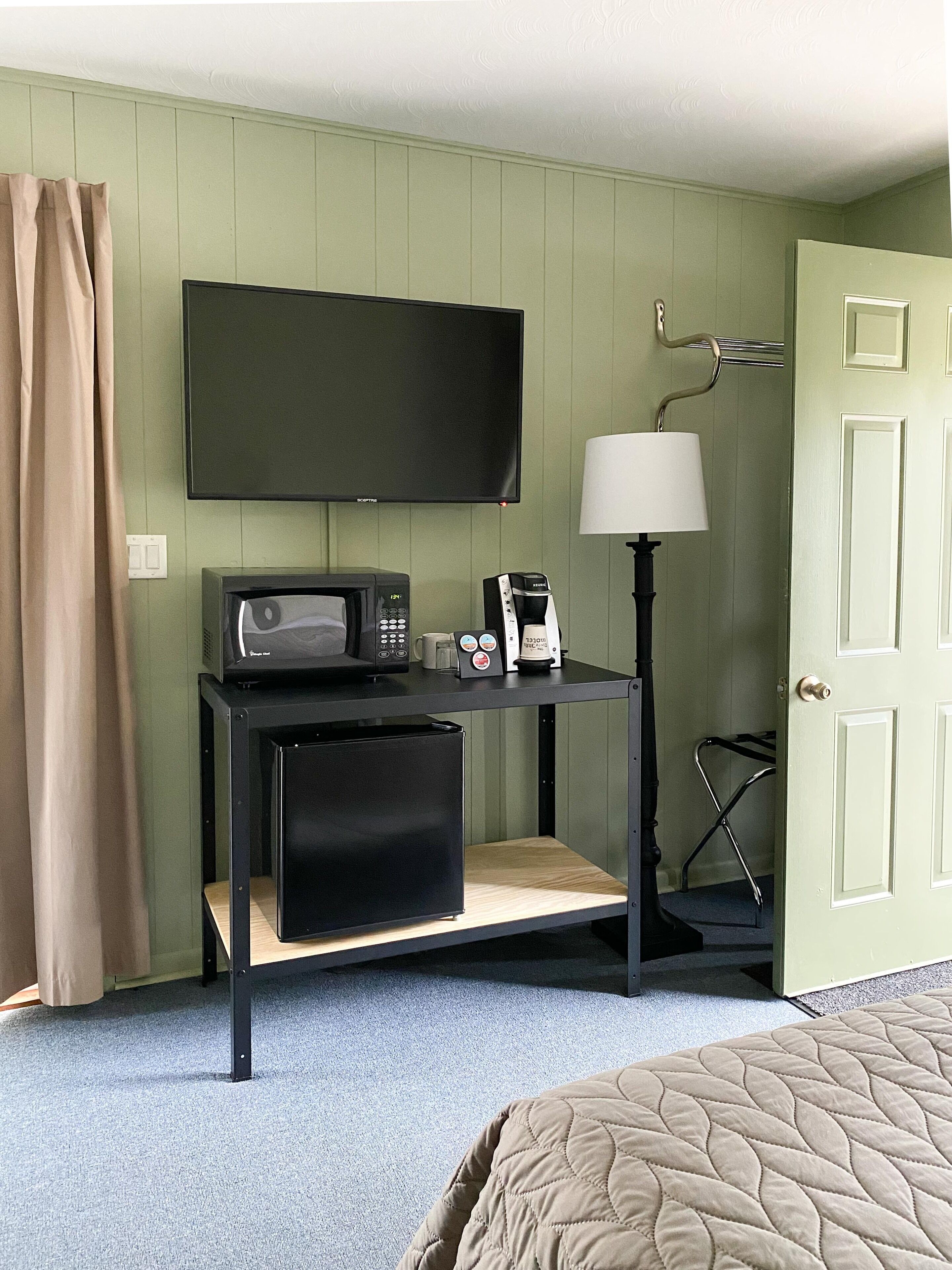 A hotel room with a bed, a desk with a television, a coffee maker, and a lamp.