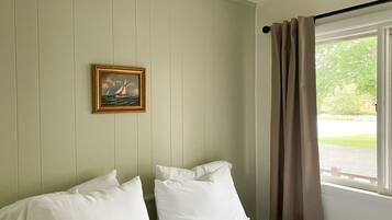 A room with a bed, a framed picture on the wall, and a window with curtains.