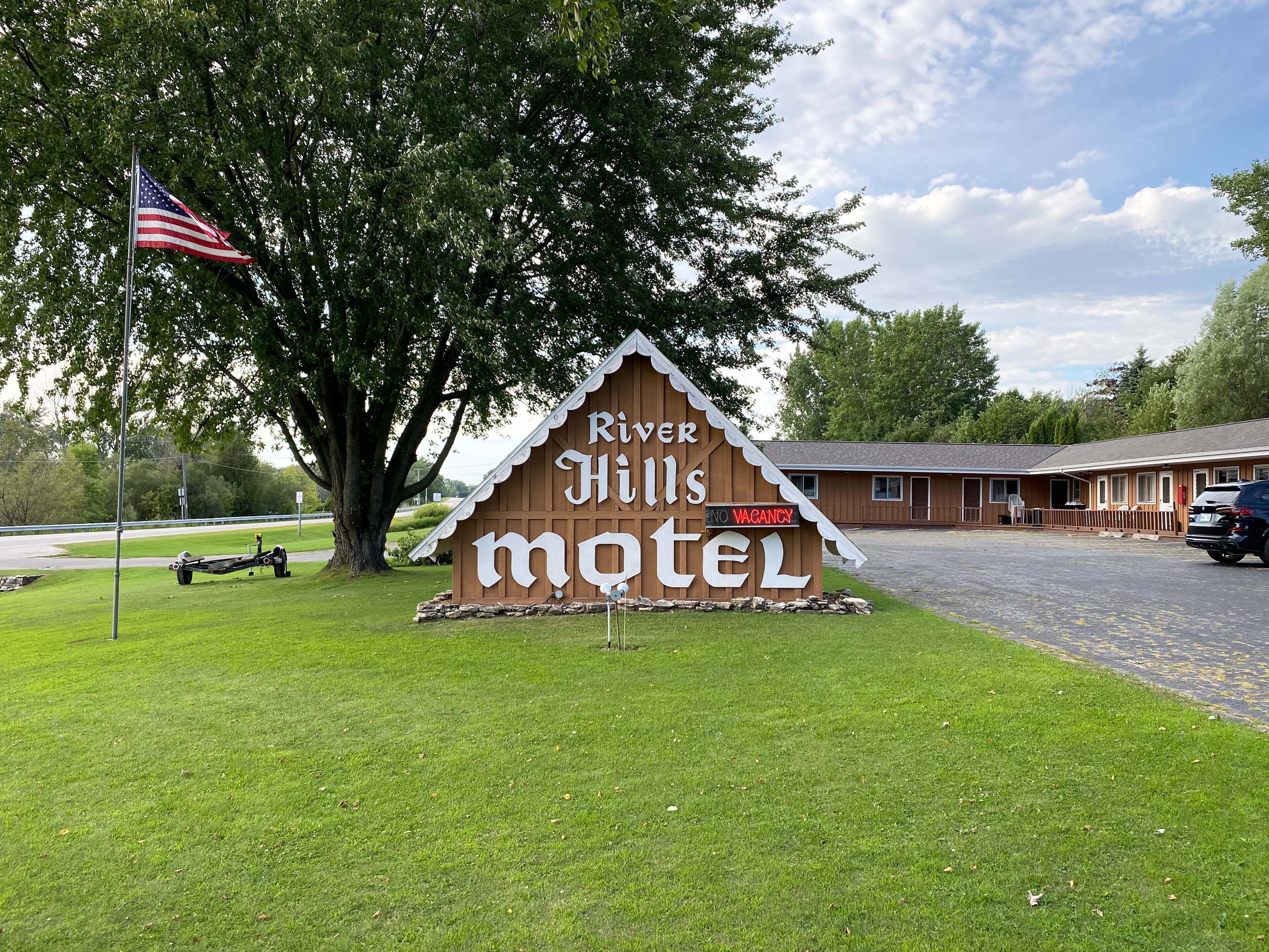 A wooden sign for River Hills Motel with a flagpole and a tree in the foreground.