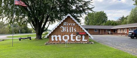 A wooden sign for River Hills Motel with a flagpole and a tree in the foreground.
