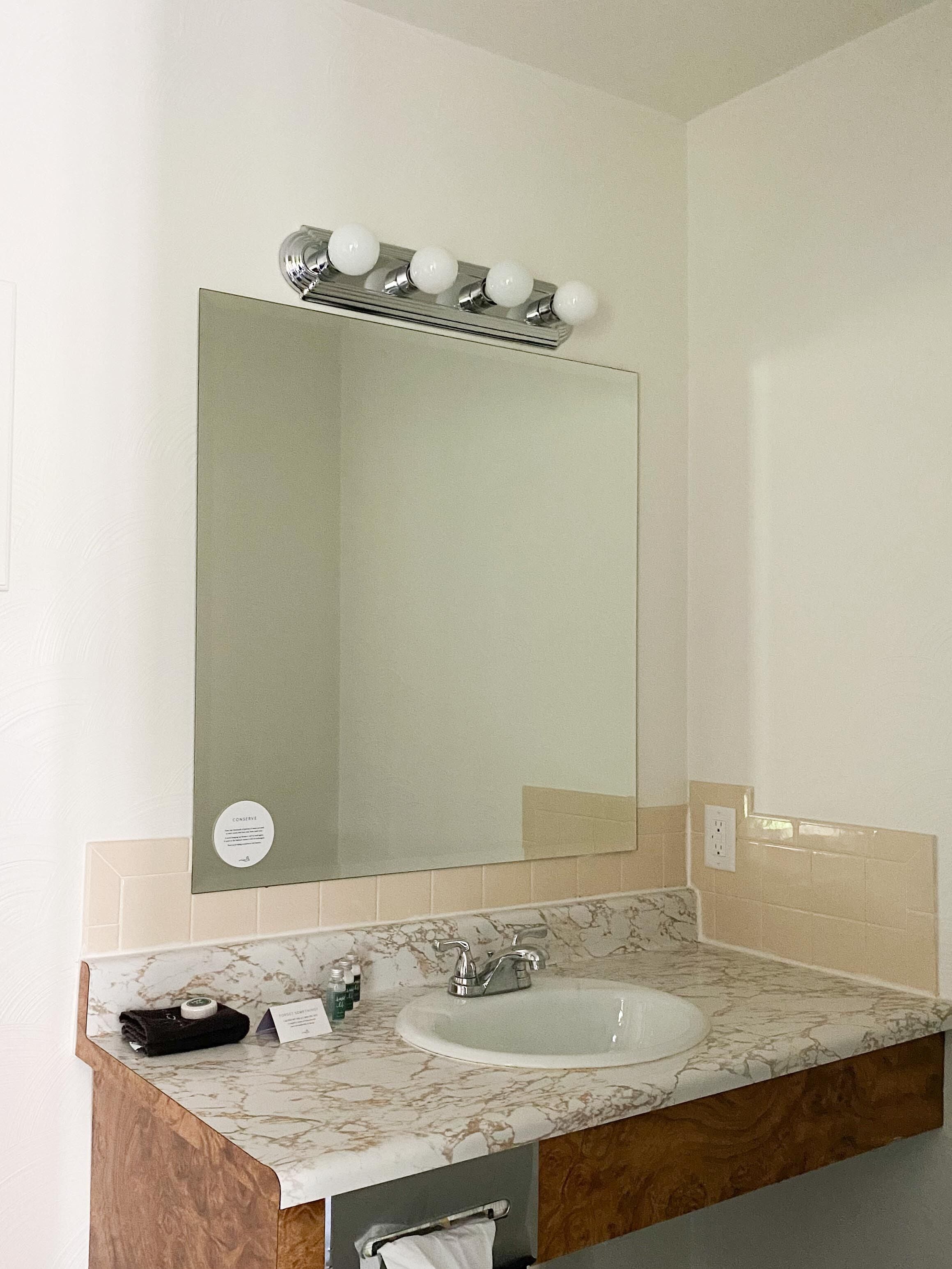 Un bagno con un ampio specchio, un lavabo e un mobile contenitore con piano in marmo.