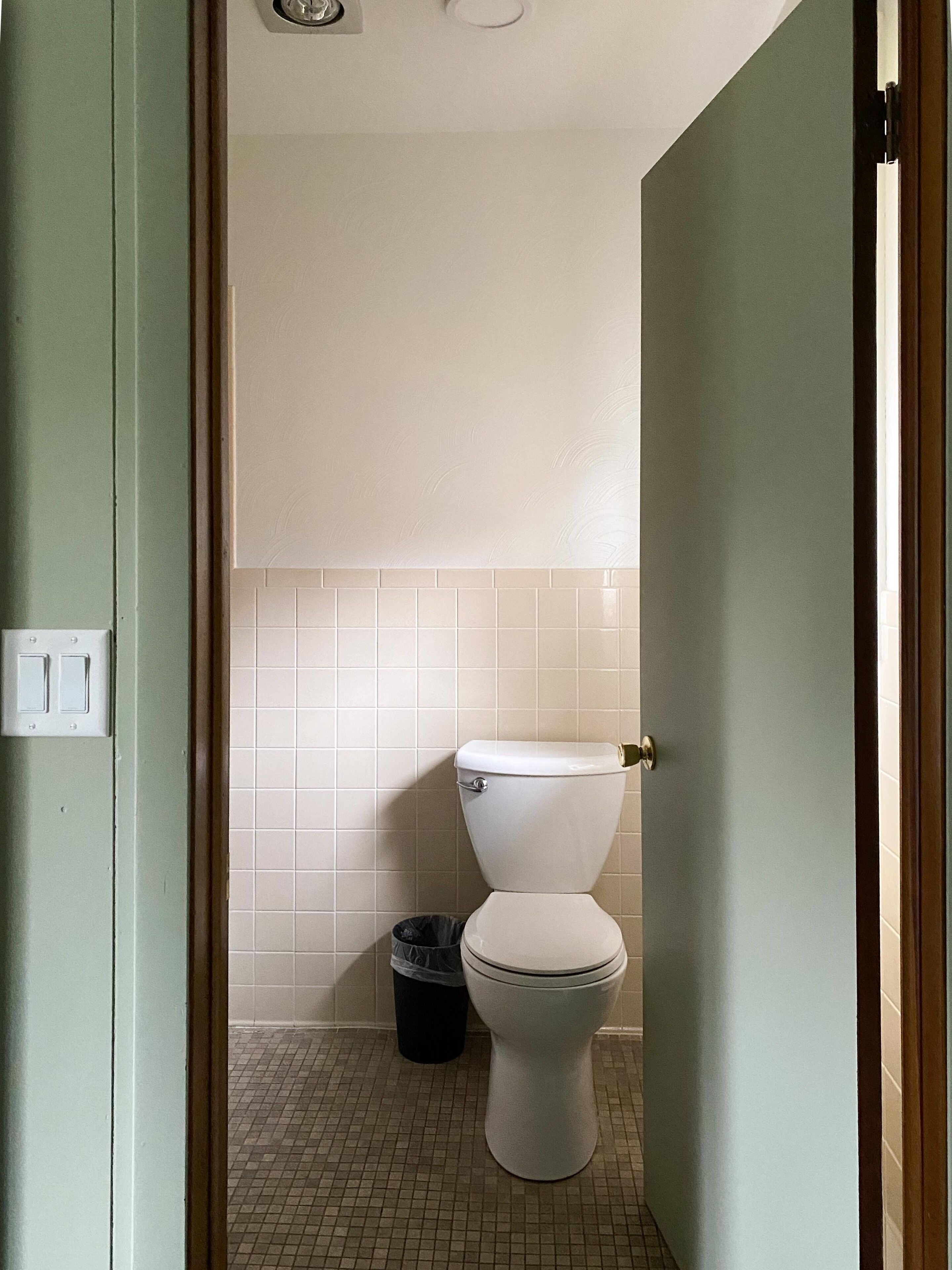 Ein kleines, sauberes Badezimmer mit Toilette, Mülleimer und Fliesenwand.