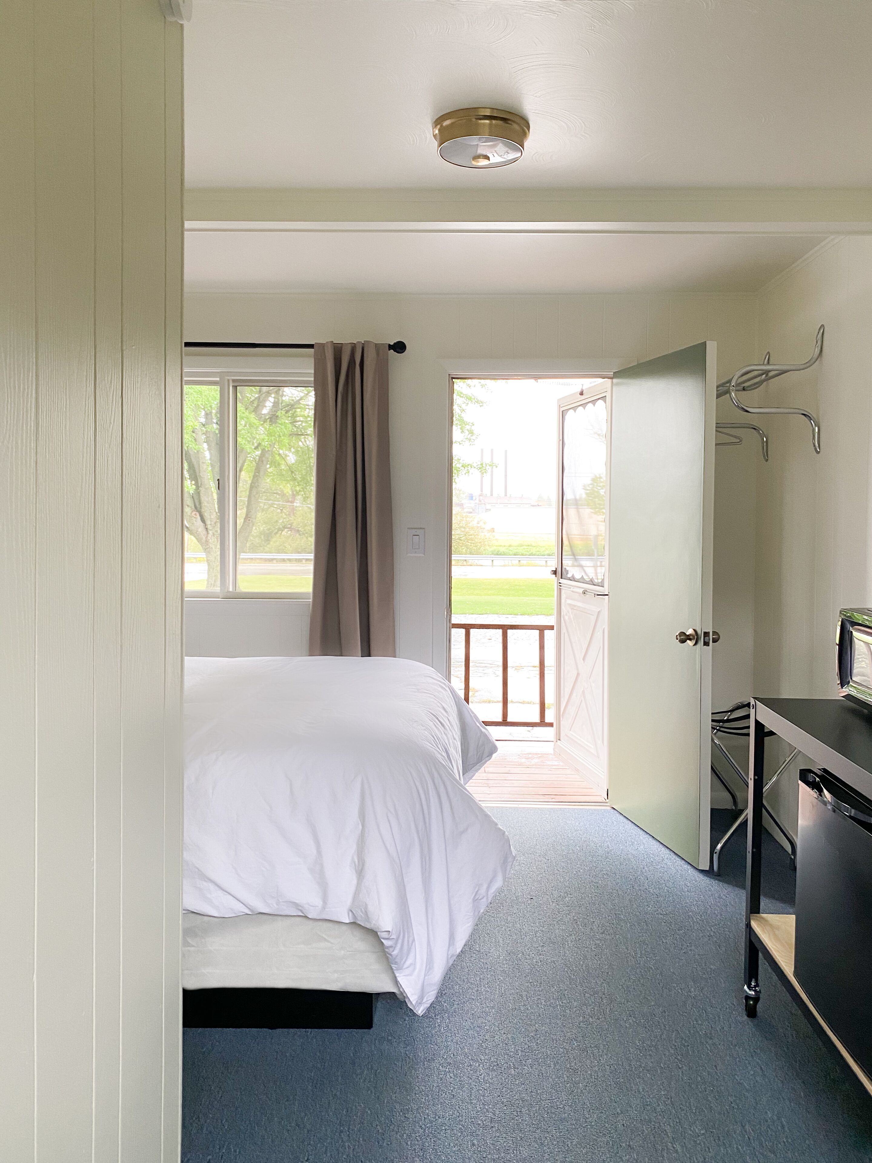 A bedroom with a bed, a desk, and a window with curtains.