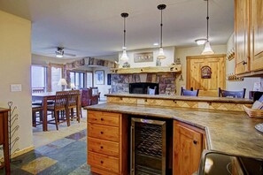 A kitchen with a stone fireplace, wooden cabinets, and a built-in wine cooler.