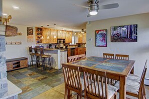 A kitchen with wooden cabinets, a dining table, and bar stools. - Amazing Summer Views! Hot Tub, Grill, 2 King Suites, Covered Parking & Scenic Decks! (Steamboat Springs)
