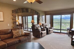 A spacious living room with a stone fireplace, leather sofas, and a view of a mountainous landscape through large windows. - Amazing Views-Hot Tub-2 King Suites-Coverd Parking (Steamboat Springs)