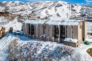 A multi-story hotel with a flat roof, surrounded by snow-covered mountains and a ski slope. - Amazing Summer Views! Hot Tub, Grill, 2 King Suites, Covered Parking & Scenic Decks! (Steamboat Springs)
