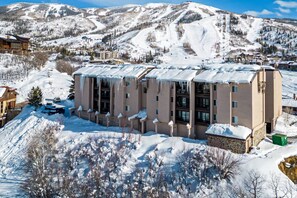 A multi-story hotel with a snow-covered roof, situated in a mountainous area with ski slopes in the background.