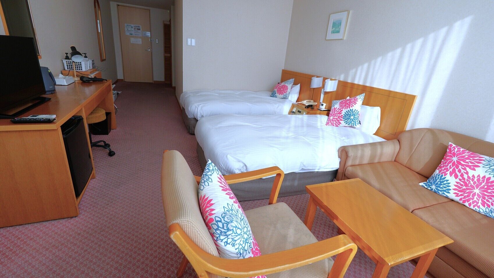 A hotel room with a bed, two chairs, a desk with a computer, and a TV.