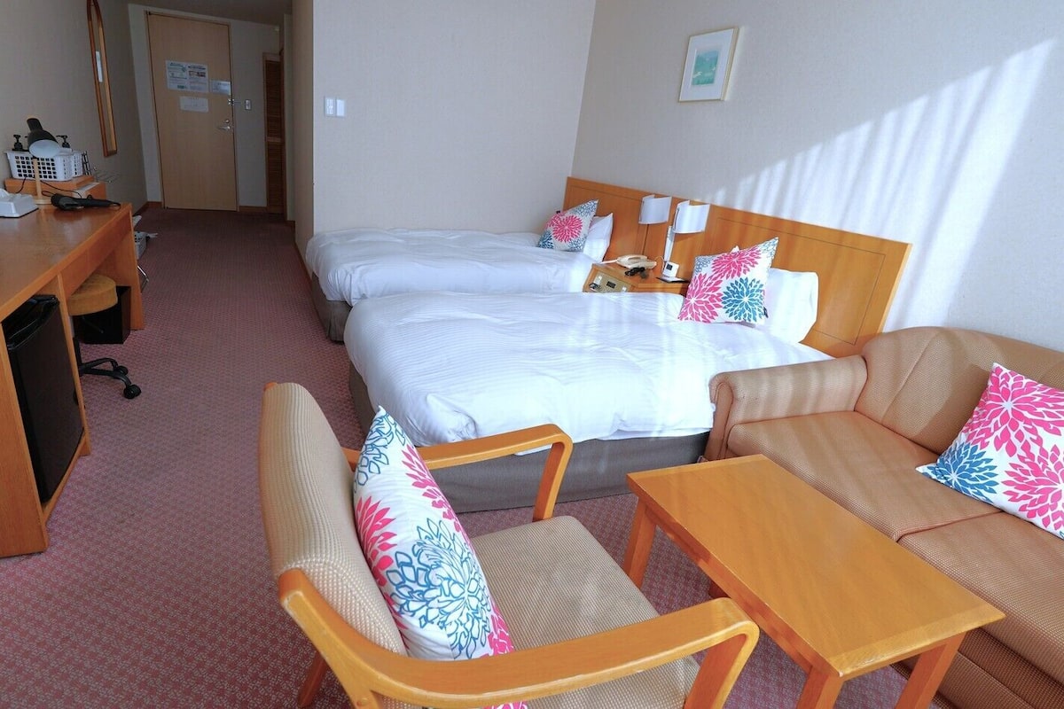A hotel room with a bed, two chairs, a desk with a computer, and a TV.
