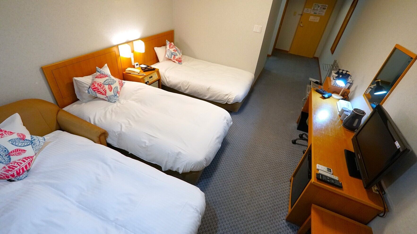 A hotel room with two beds, a desk with a computer and phone, and a mirror.
